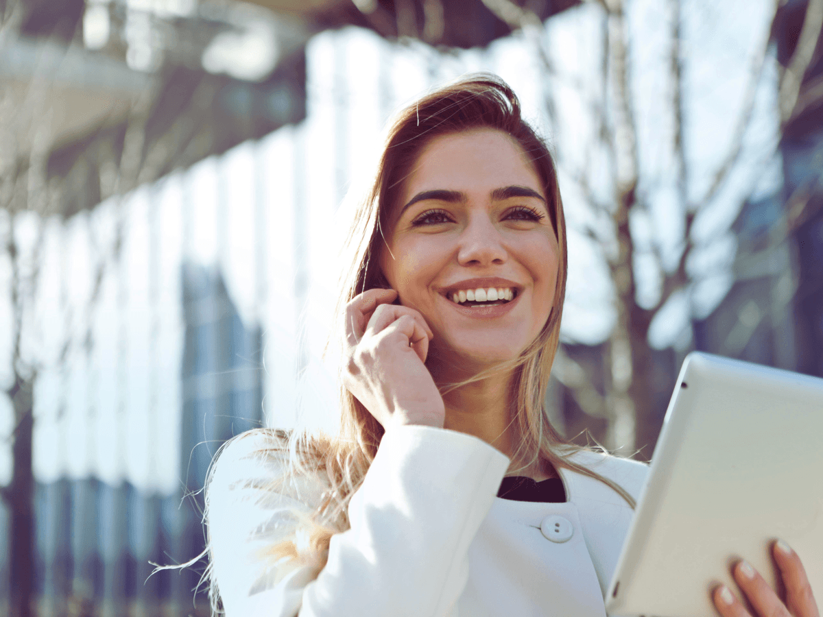 Smiling businesswoman holding a tablet outdoors reviewing brand strategy plans in a modern corporate environment